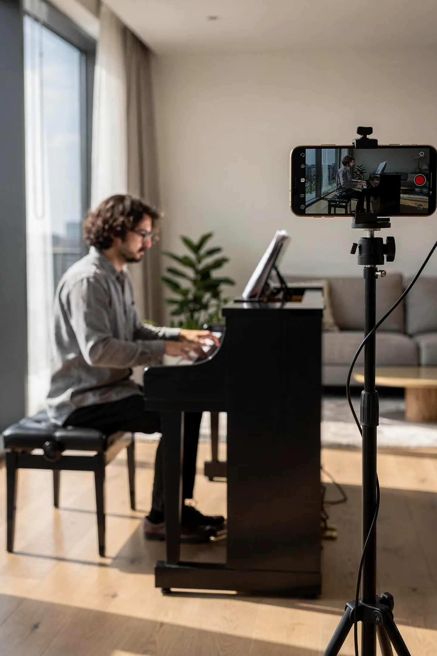 A learner practicing piano while a phone on a tripod watches and coaches.